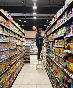 Staff member checking products on supermarket shelves in a grocery store aisle.